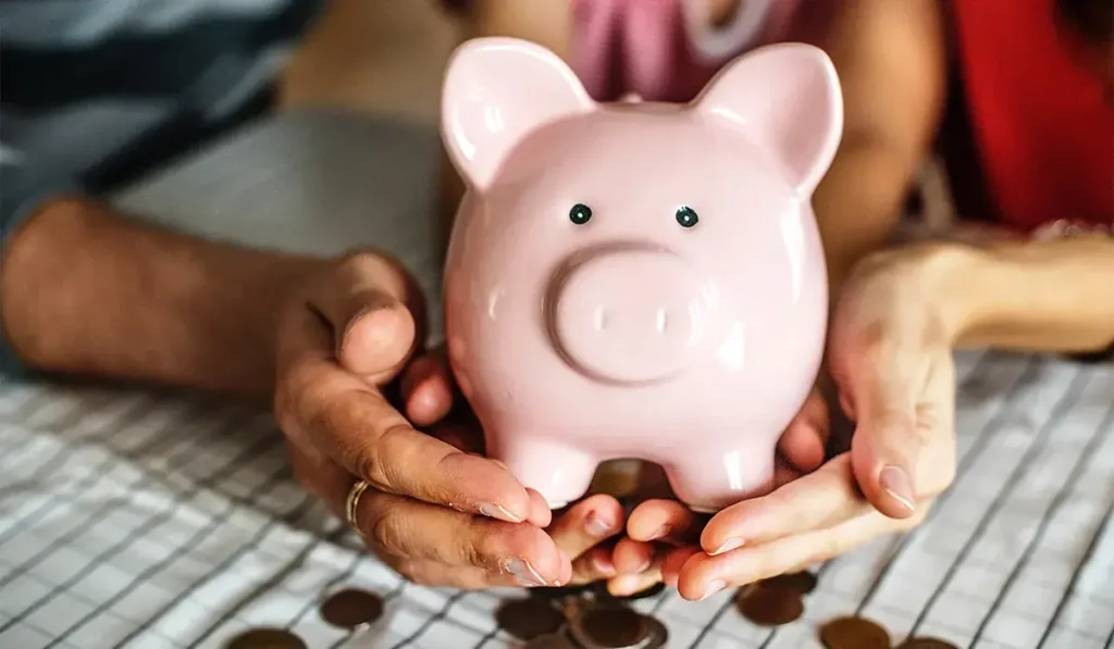 Adult holding a child's hands with a large piggy bank on top.