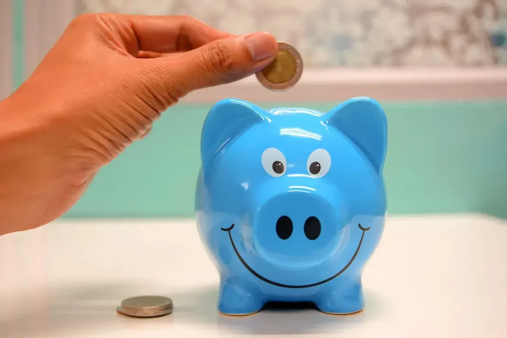 Hand holding a coin above a smiling piggy bank.