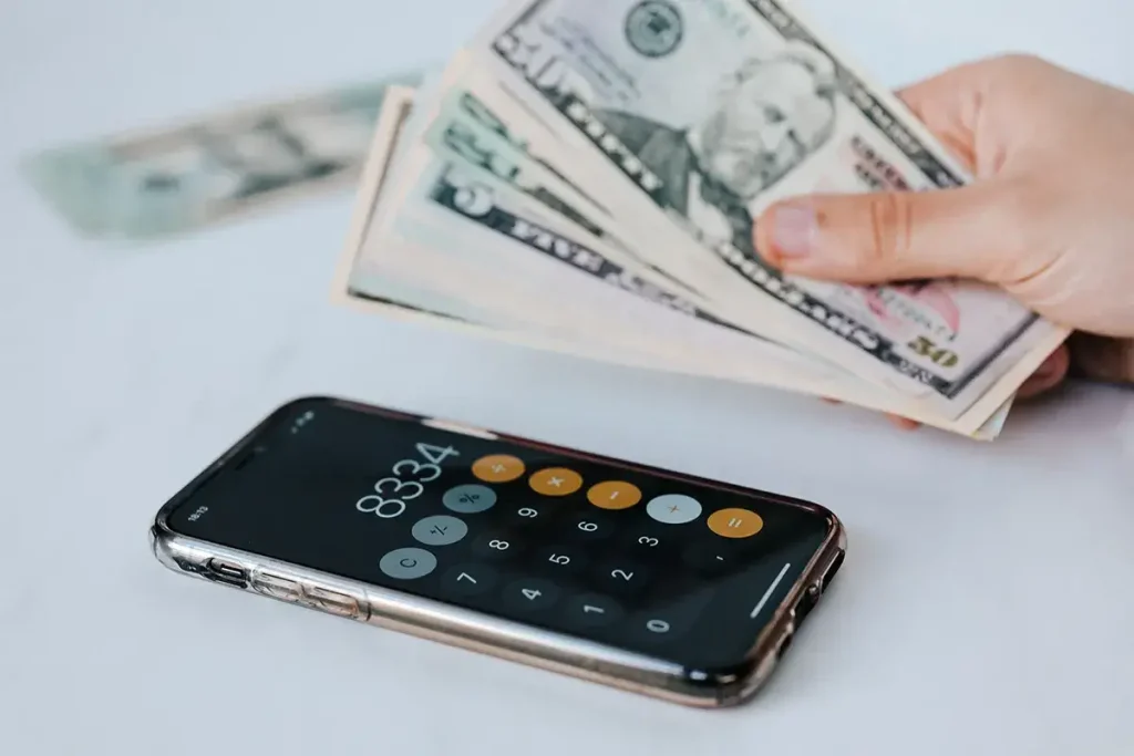 Handful of cash and a phone being used in as a calculator.