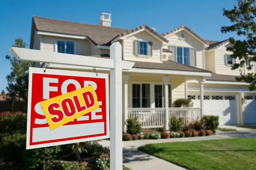 A home with a for sale sign in front covered in a sold sticker.