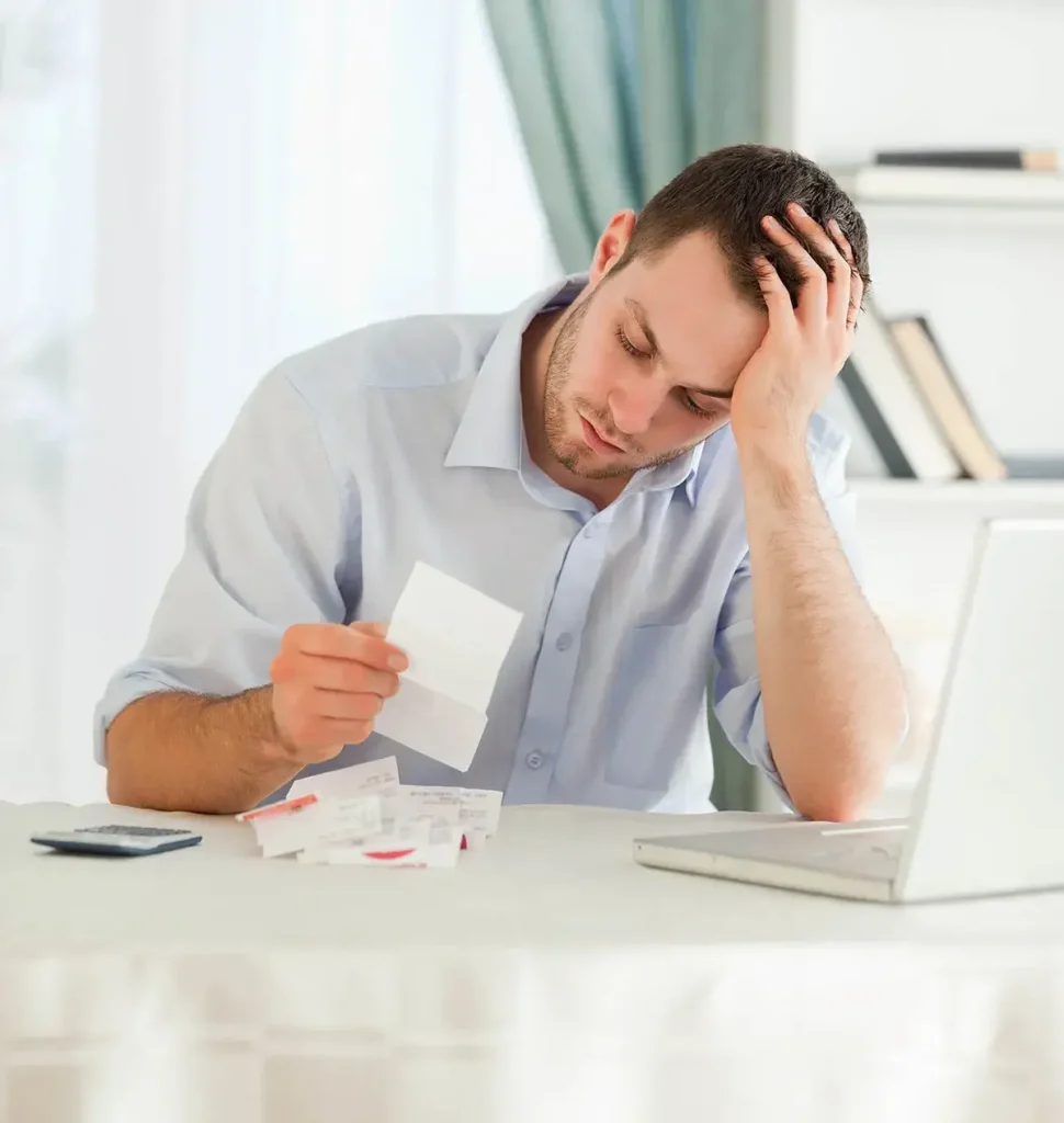 Person bent over in stress at a table looking at receipts.