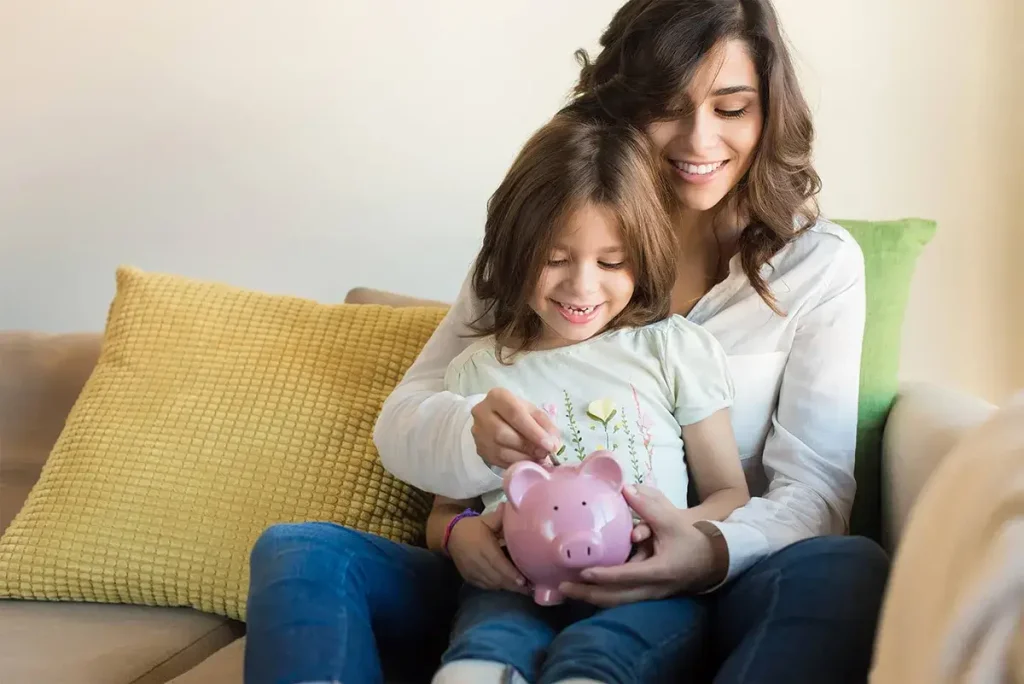 Mother and child sitting on a couch putting money into a piggy bank.