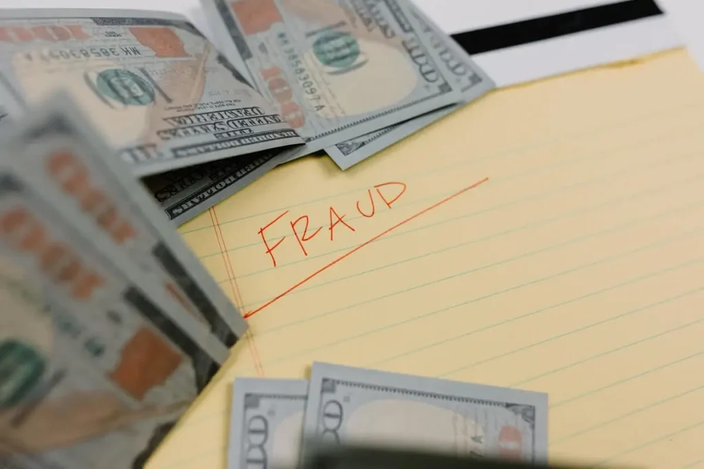 Fraud written on a pad of paper with $100 bills falling around it.