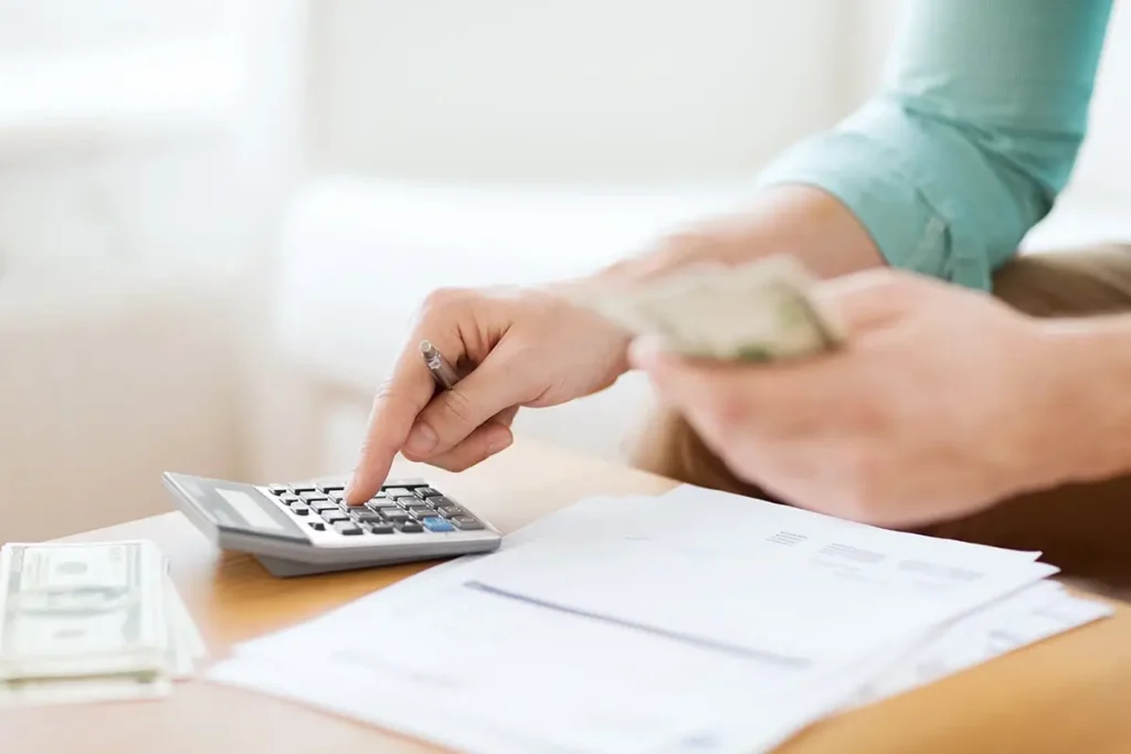 Person using a calculator, holding cash, and looking at paperwork.