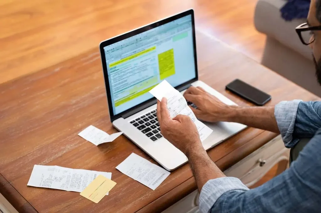 Man entering receipts into a spreadsheet on a laptop.