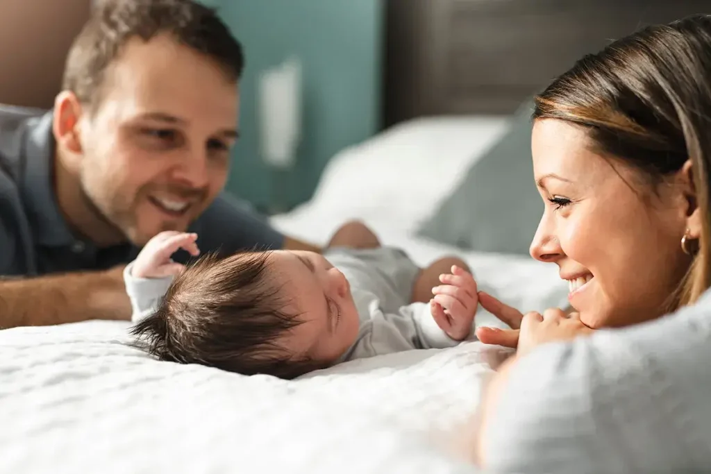 New parents on either side of a bed looking at their newborn in the middle.