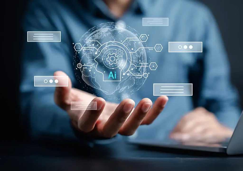 A person holds out their hand with a glowing AI graphic hovering above it, showing a head, gears, and digital icons, symbolizing artificial intelligence and technology. A laptop is visible in the background.