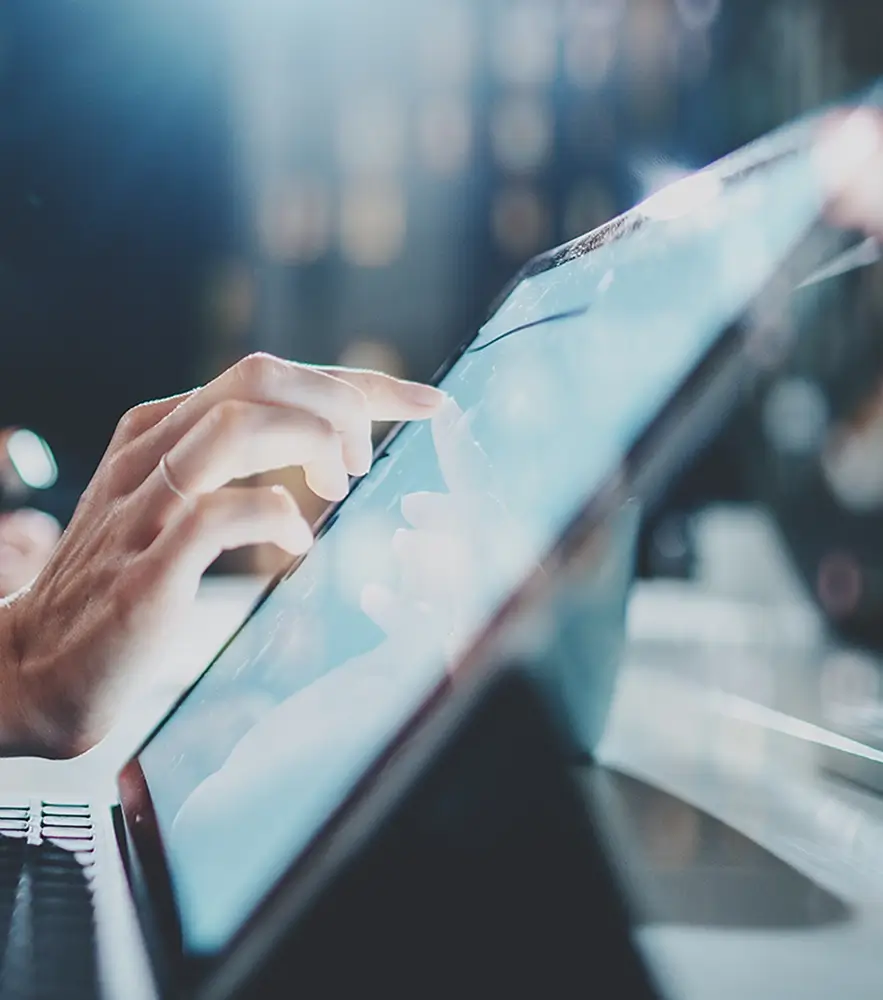 Close-up of a hand interacting with a laptop, in a brightly lit workspace with a blurred background.