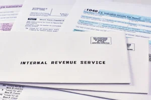 Three envelopes from the Internal Revenue Service lie on 1040, Schedule D form 1040 and 1040a tax forms