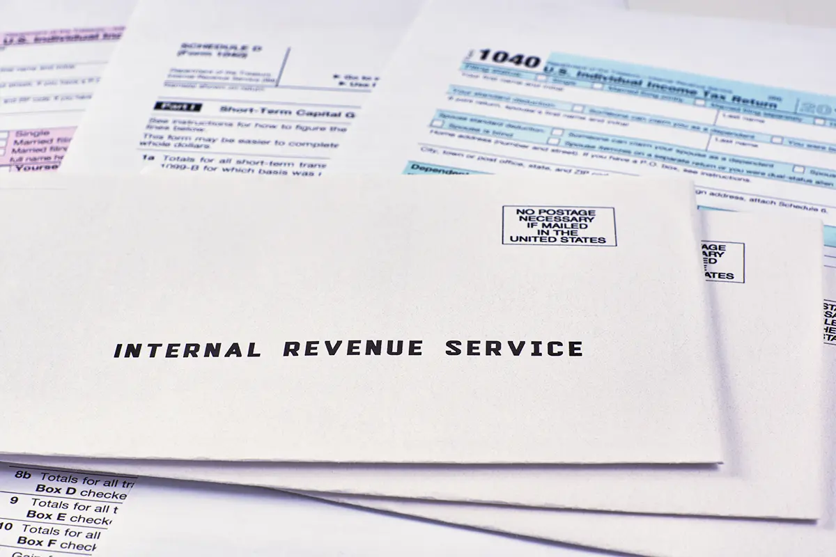 Three envelopes from the Internal Revenue Service lie on 1040, Schedule D form 1040 and 1040a tax forms