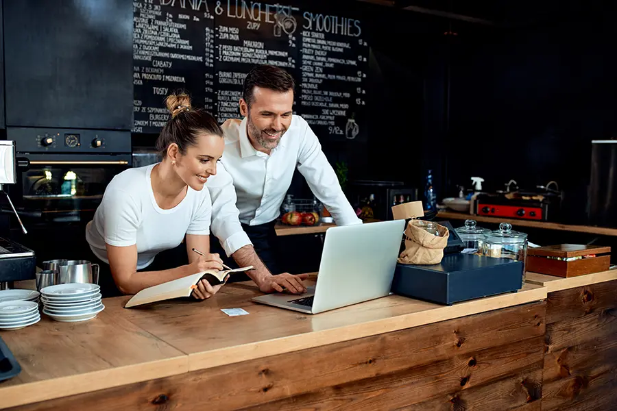 Happy small business owners working on finances with laptop at cafe